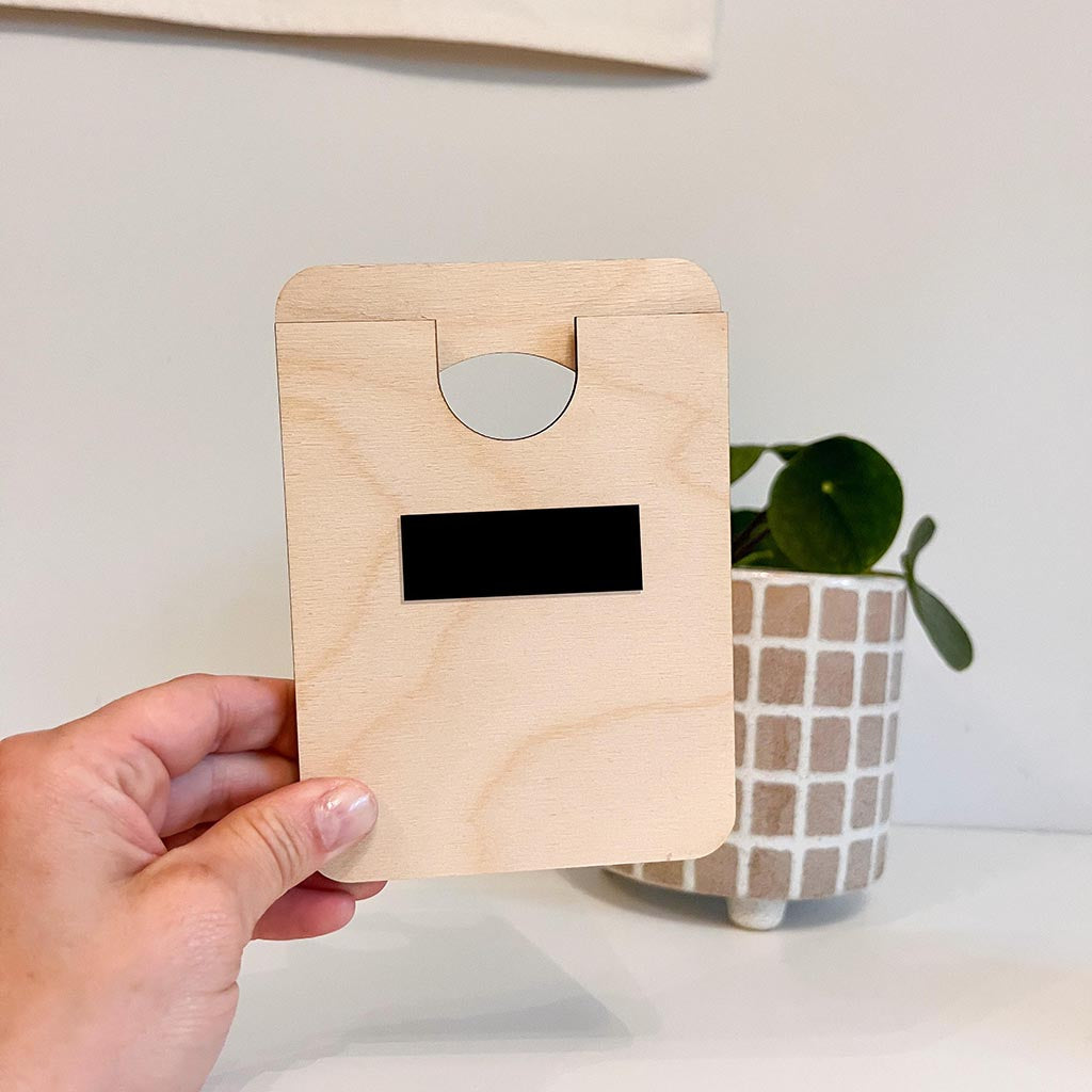 Hand holding a wooden card with a black label against a neutral background