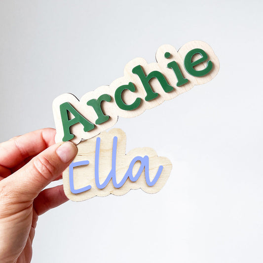 Hand holding cut-out letters spelling 'Archie' and 'Ella' against a light background