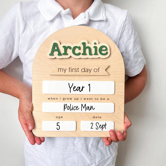 Child holding a wooden plaque with 'Archie' and personalized text against a plain background