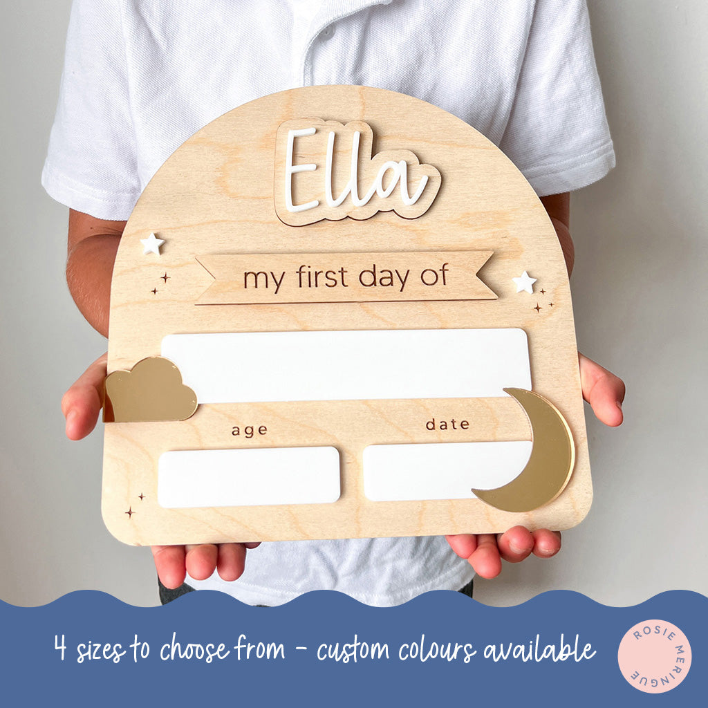 Wooden plaque with 'Ella' and 'my first day of' text, held by a person against a neutral background.