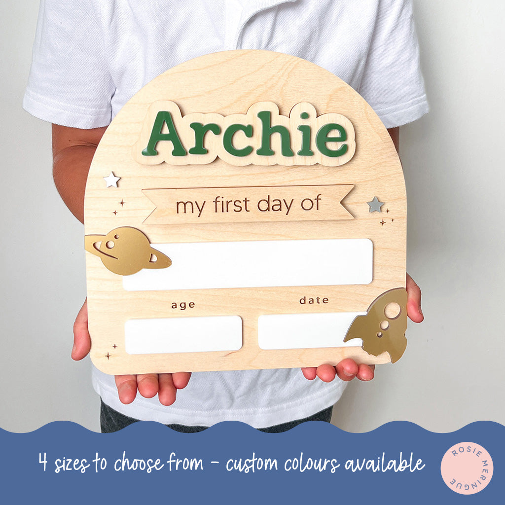 Wooden plaque with 'Archie' and space-themed decorations held by a person.