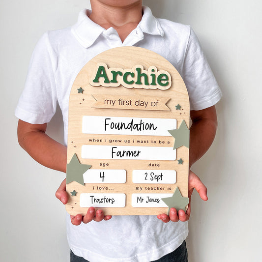 Child holding a wooden plaque with personalized text on a plain background