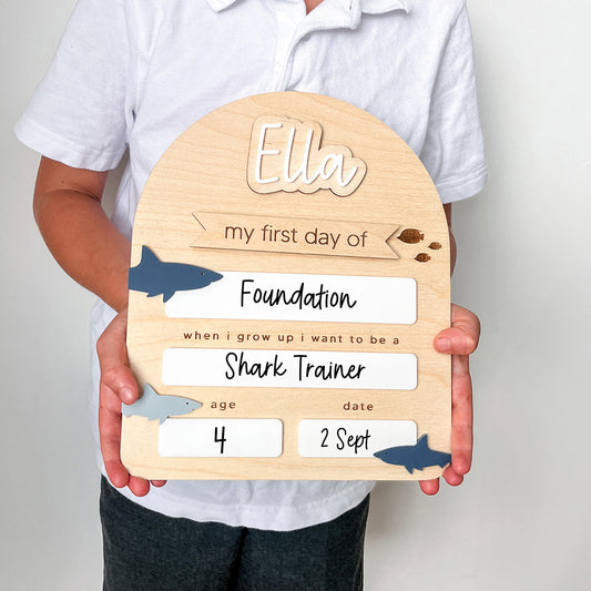 Child holding a wooden plaque with personalized text and shark illustrations.