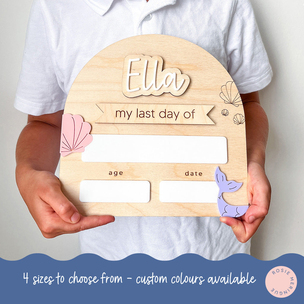 Wooden plaque with 'Ella' and space for 'my last day of' text, held by a person.