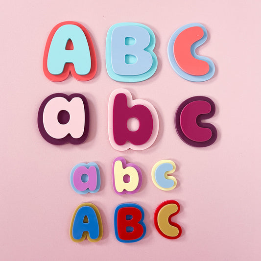 Three rows of colorful alphabet letters for children, showing uppercase and lowercase letters A, B, and C in various pastel and bright colors, arranged on a solid pink background.