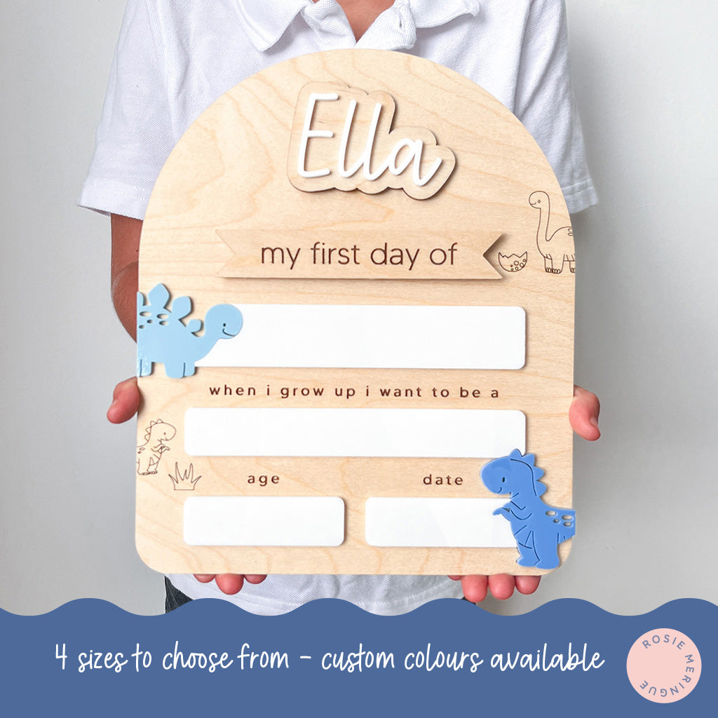 Wooden plaque with cutouts for 'my first day of' and 'when I grow up I want to be a' with dinosaur illustrations, held by a person.