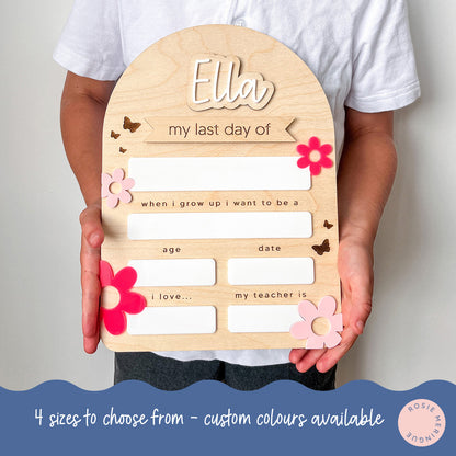 Wooden board with cutouts held by a person, personalized for 'Ella's last day of school'.