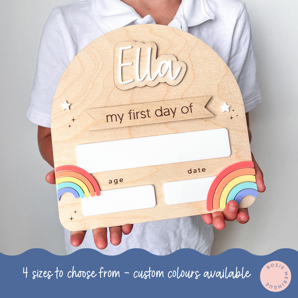 Wooden plaque with 'Ella' and 'my first day of' text, held by a person against a plain background.