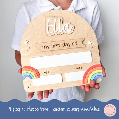 Wooden plaque with 'Ella' and 'my first day of' text, held by a person against a plain background.