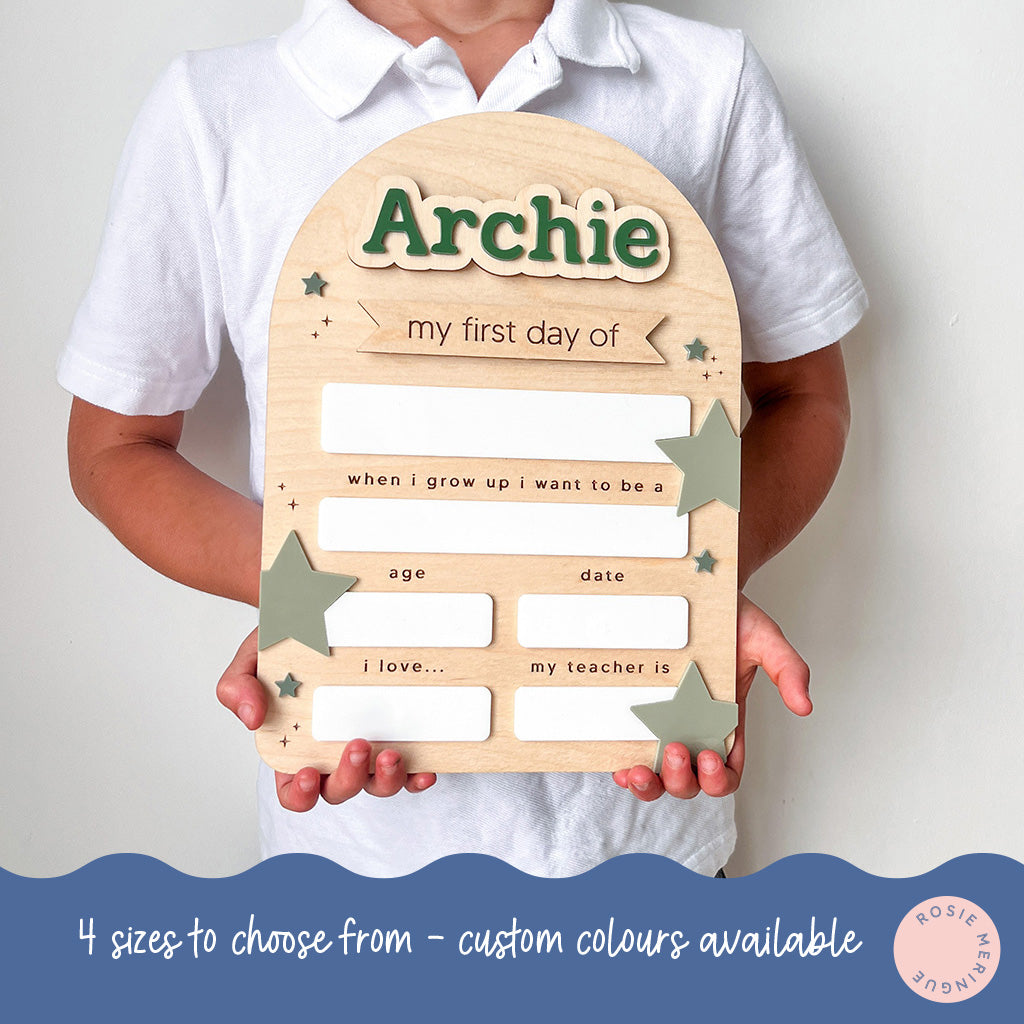 Child holding a wooden plaque with 'Archie' on it, designed for the first day of school.