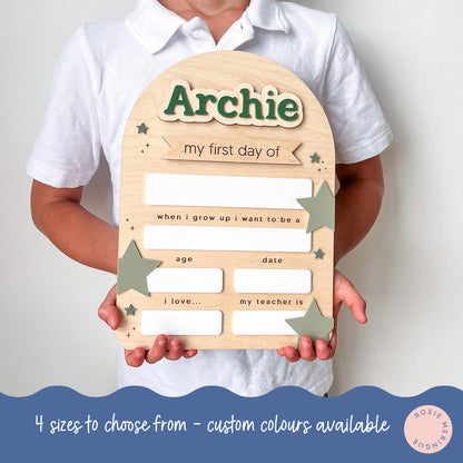Child holding a wooden plaque with 'Archie' on it, designed for the first day of school.