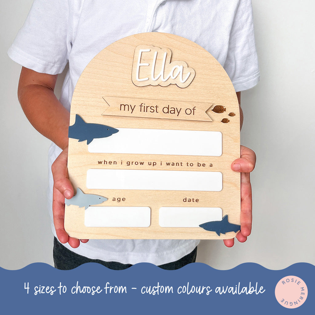 Wooden plaque with 'Ella' engraved, held by a person, with text and shark illustrations.