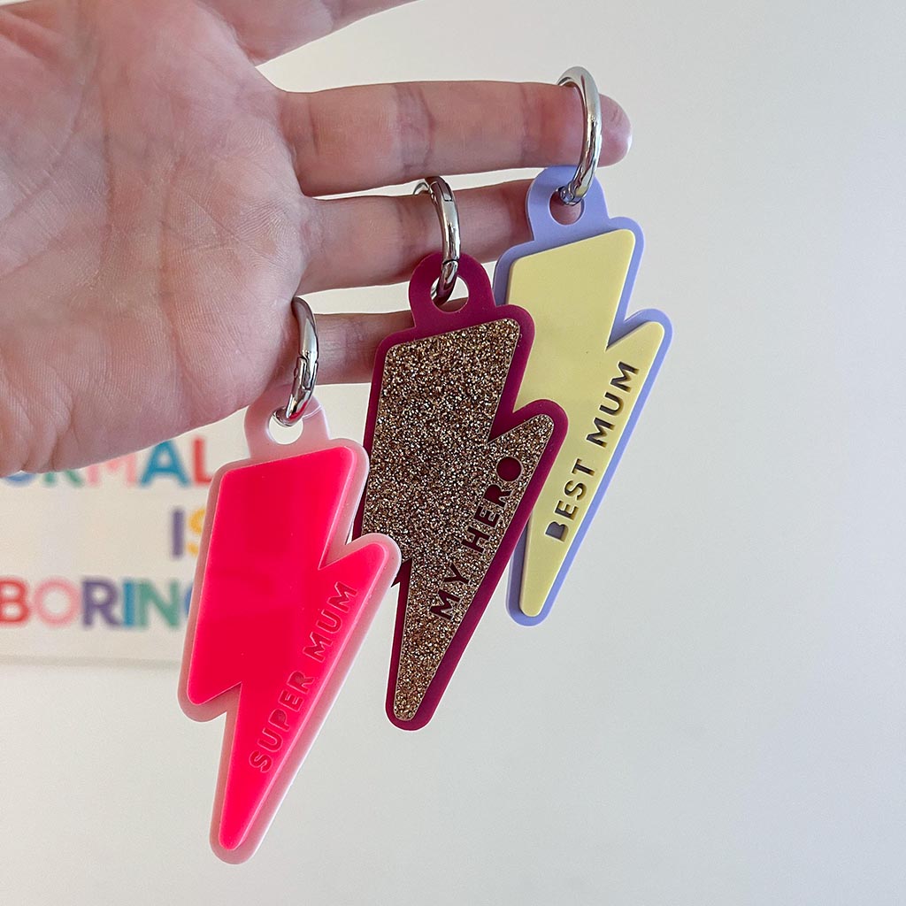 Three colorful keychains shaped like lightning bolts held by a hand against a light background.