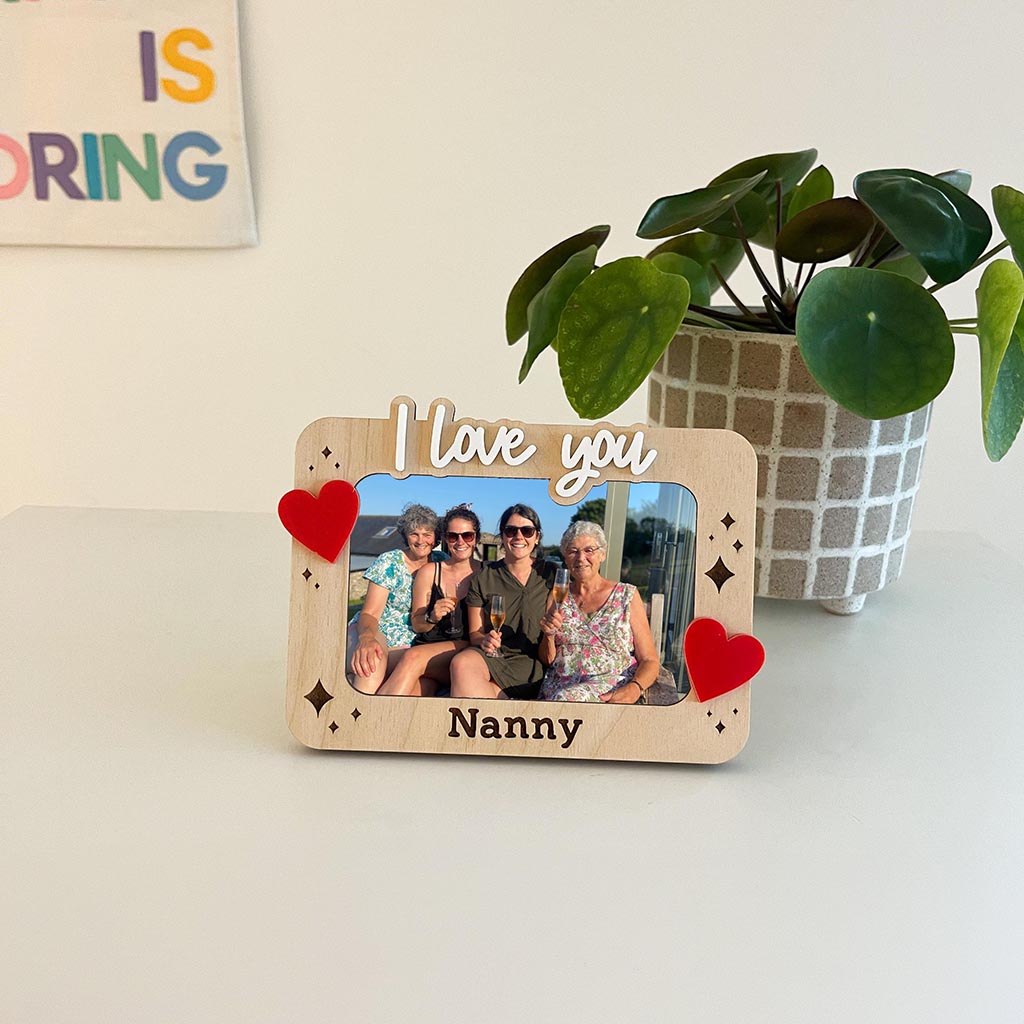 Wooden photo frame with 'I love you Nanny' text, family photo, and red hearts on a light surface.