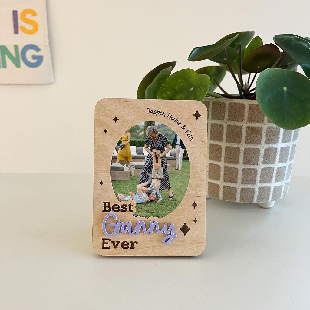 Wooden photo frame with family photo and 'Best Ganny Ever' text, placed on a surface with a plant in the background.