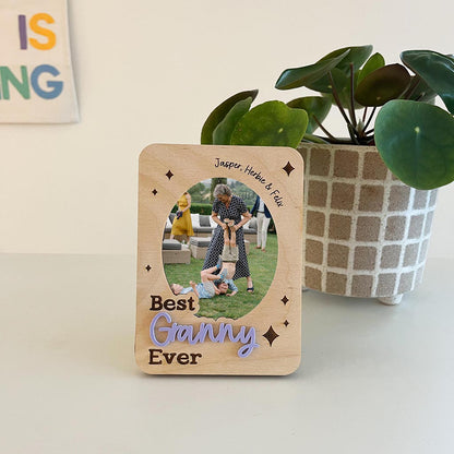 Wooden photo frame with family photo and 'Best Ganny Ever' text, placed on a surface with a plant in the background.