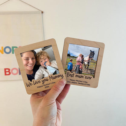 Two wooden photo frames with engraved text and images, held by a hand against a light background.