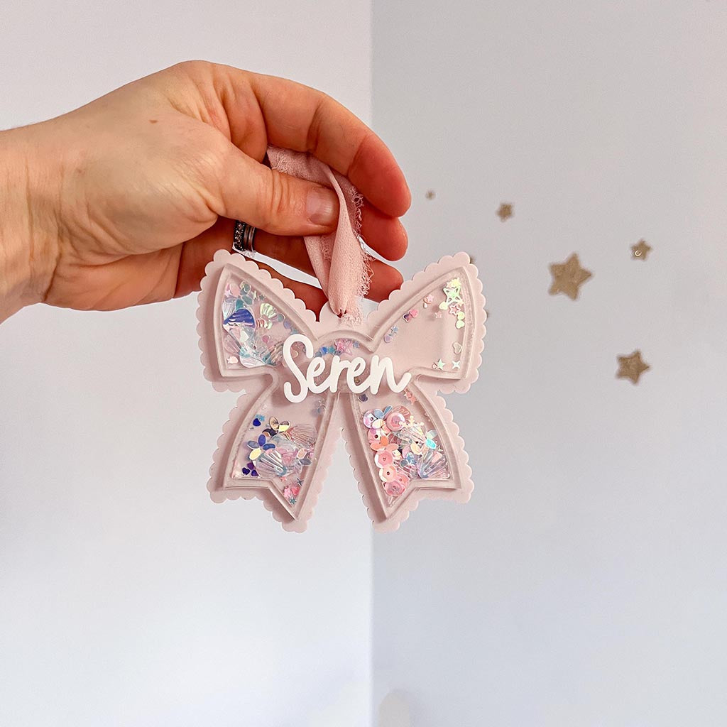Pink decorative bow with 'Seren' text held by a hand against a white background