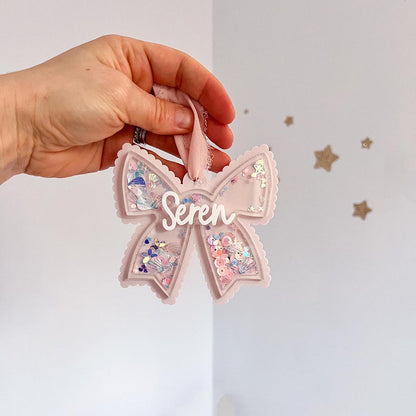 Pink decorative bow with 'Seren' text held by a hand against a white background