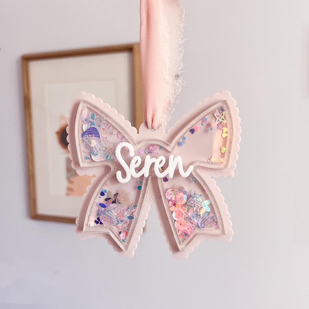 Decorative acrylic bow with glitter inside and the name 'Seren' on a light background