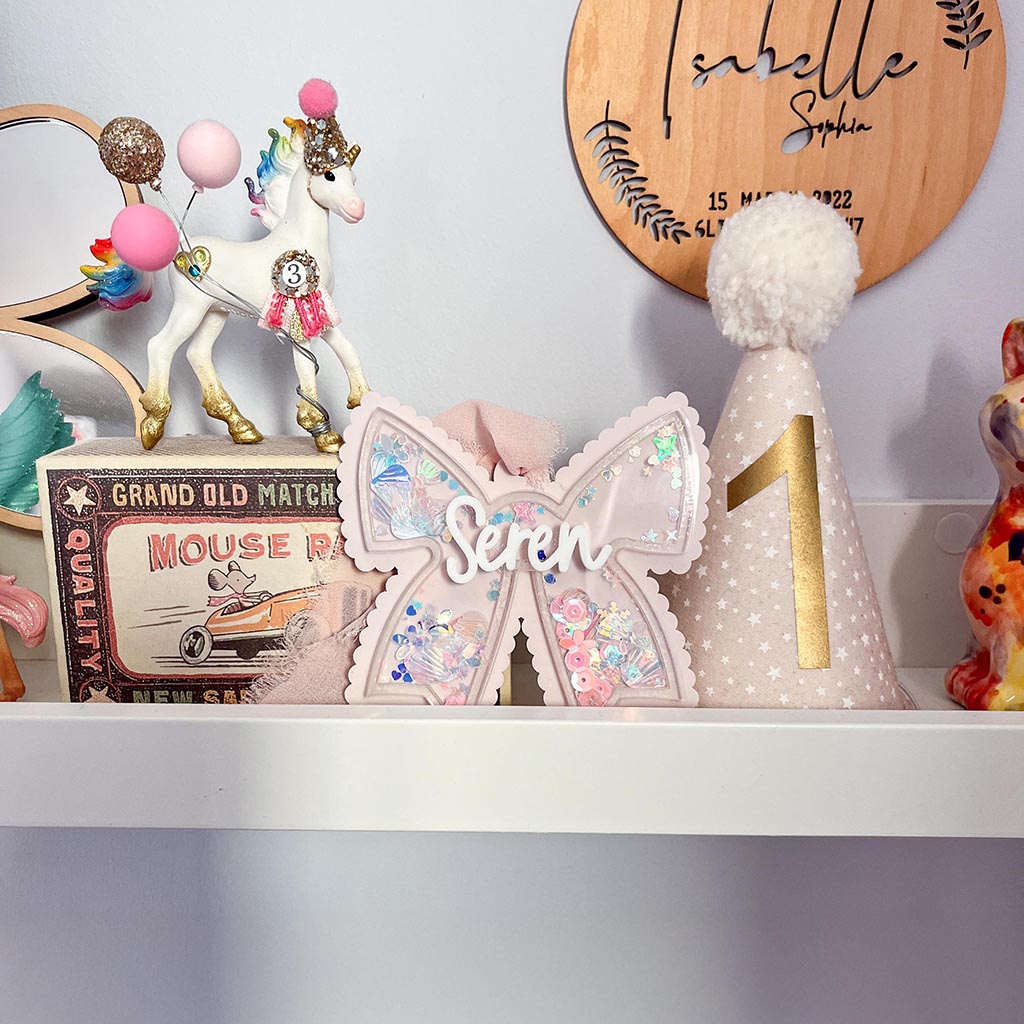Decorative acrylic bow with glitter inside and the name 'Seren' on a shelf