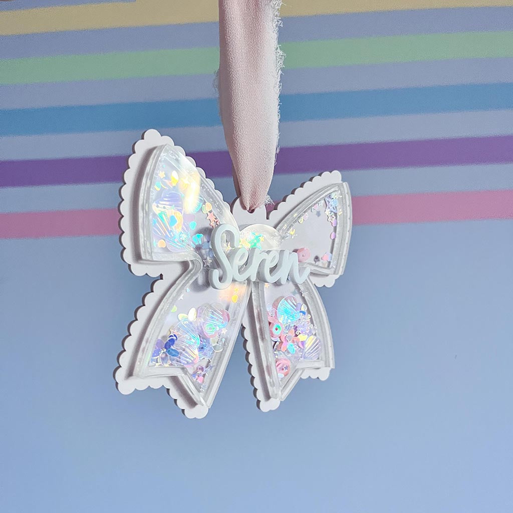Decorative acrylic bow with glitter inside and the name 'Seren' on a striped background
