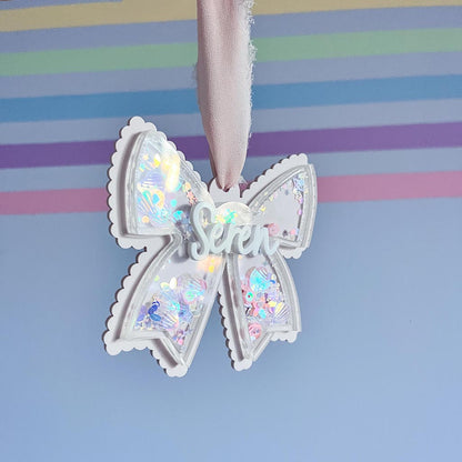 Decorative acrylic bow with glitter inside and the name 'Seren' on a striped background