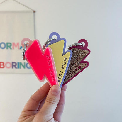 Colorful keychains with text held by a hand against a light background