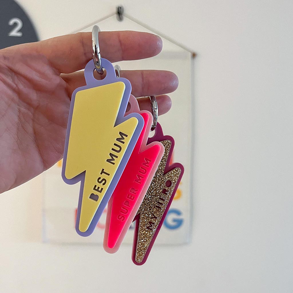 Three colorful lightning bolt-shaped keychains with text held by a hand against a blurred background.
