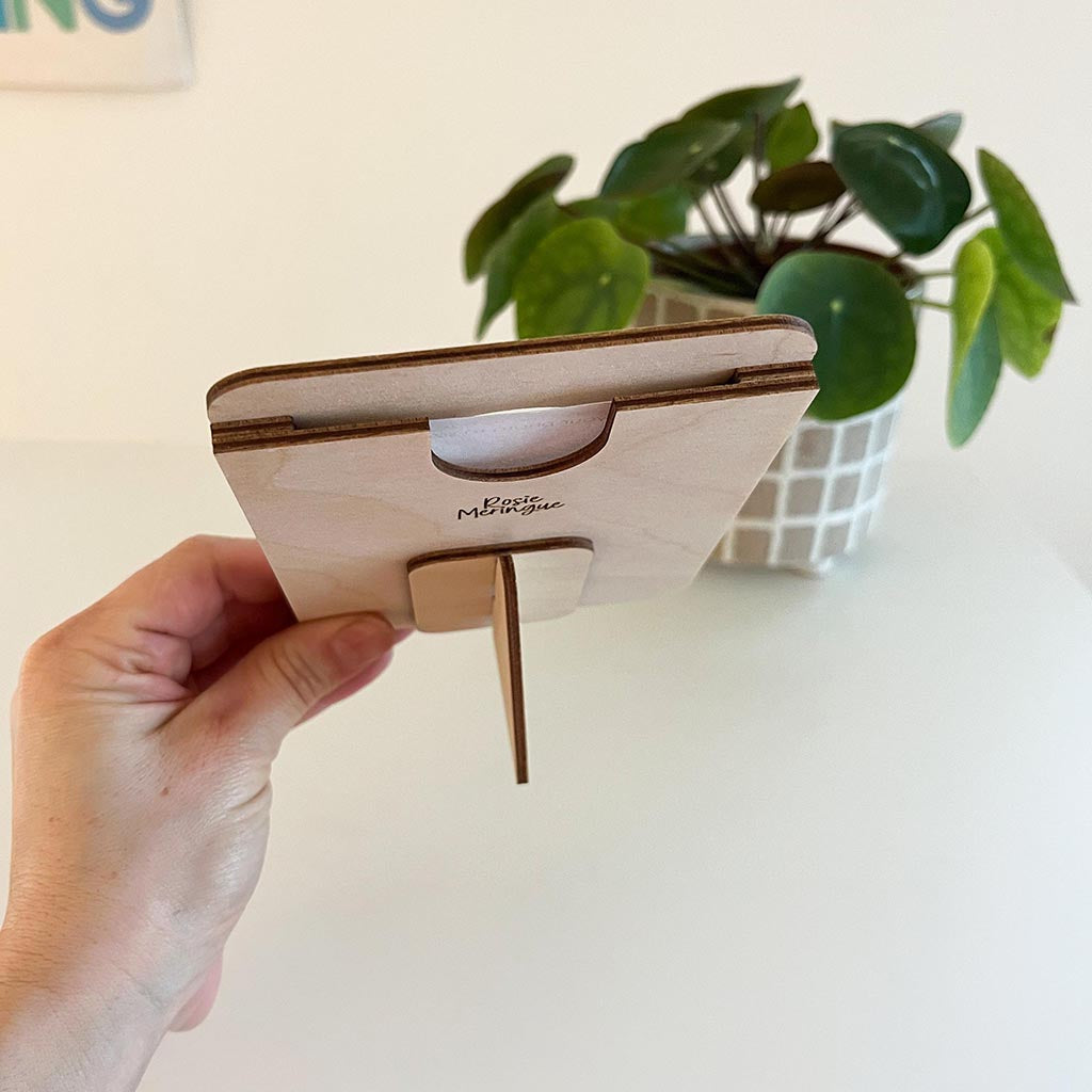 Hand holding a wooden phone stand with a plant in the background