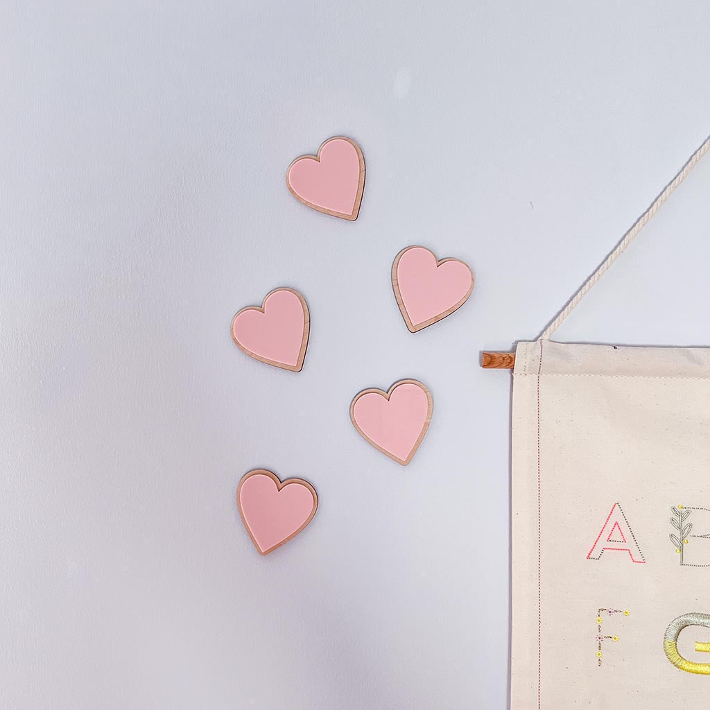 Pink wooden and acrylic heart decorations styled on a nursery wall