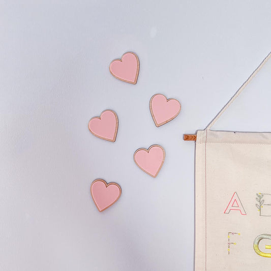 Pink wooden and acrylic heart decorations styled on a nursery wall