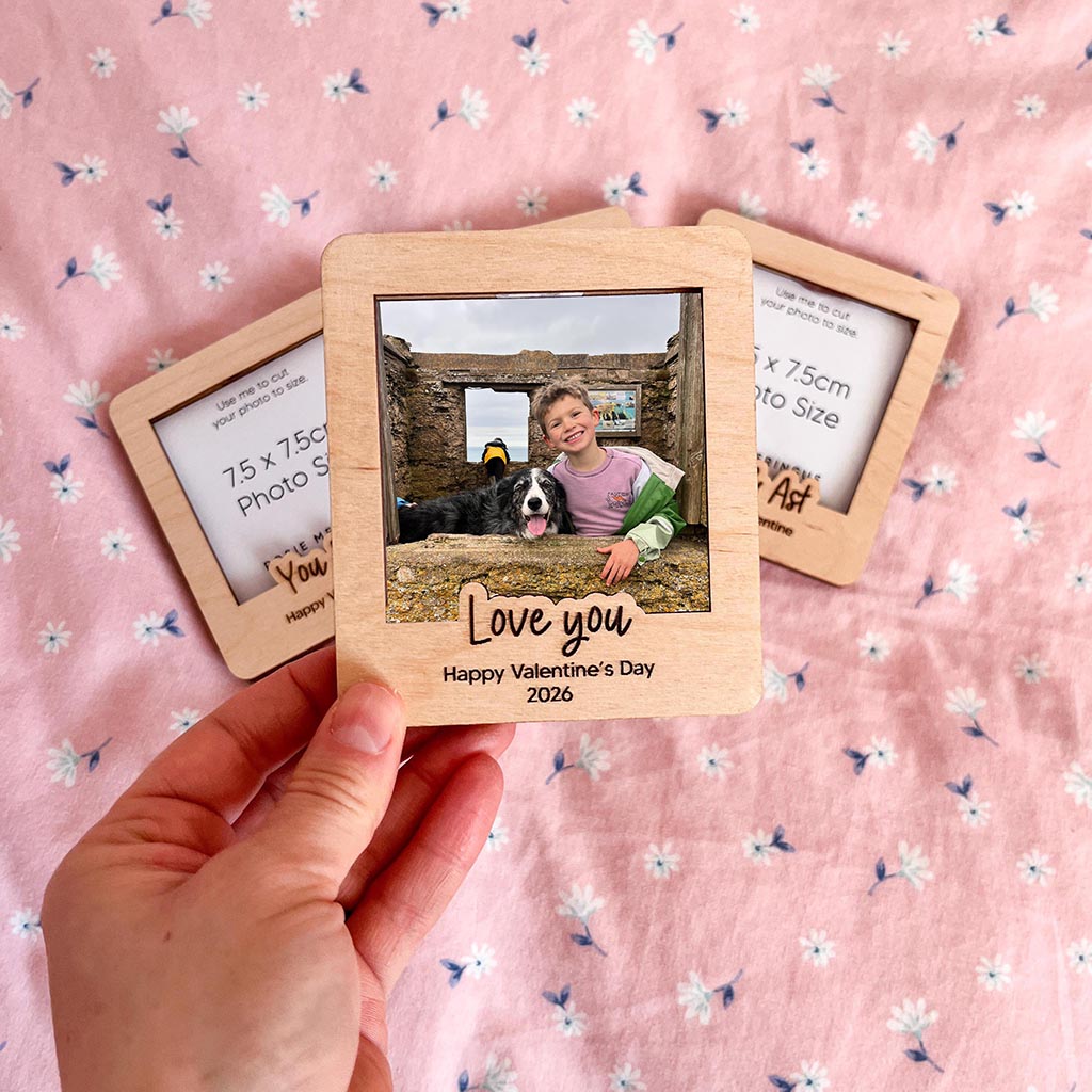 Wooden photo frame with a photo of a child and dog, held by a hand on a pink floral background.