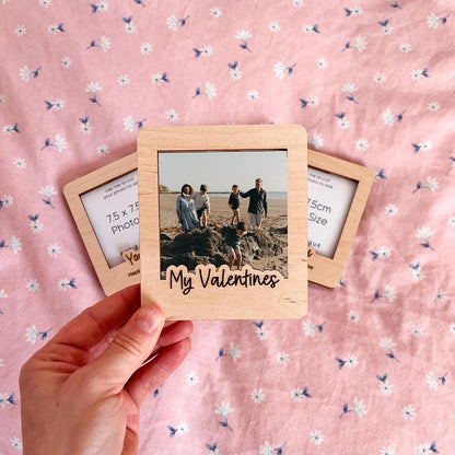 Wooden photo frame with a printed photo and 'My Valentines' text, held against a pink floral background.