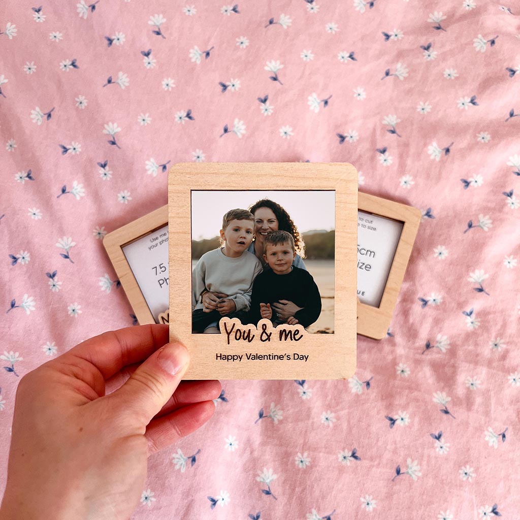 Wooden photo frame with a picture of a woman and two children, held over a pink floral fabric background.
